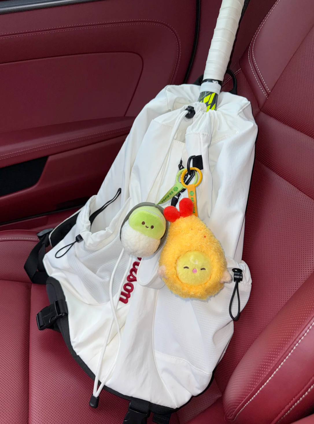 Two colorful plush tennis charms styled on a white racket bag